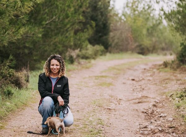 Smiling woman crouching with her dog on a scenic forest dirt path.